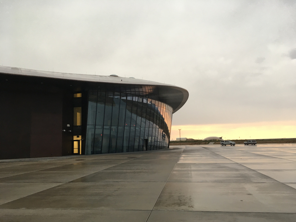 The main hangar at Spaceport America.  A cloudy evening sky is reflected in the large glass facade of the hangar.  The tarmac in front of the hangar is damp.  If I recall correctly, a thunderstorm was approaching when the picture was taken.